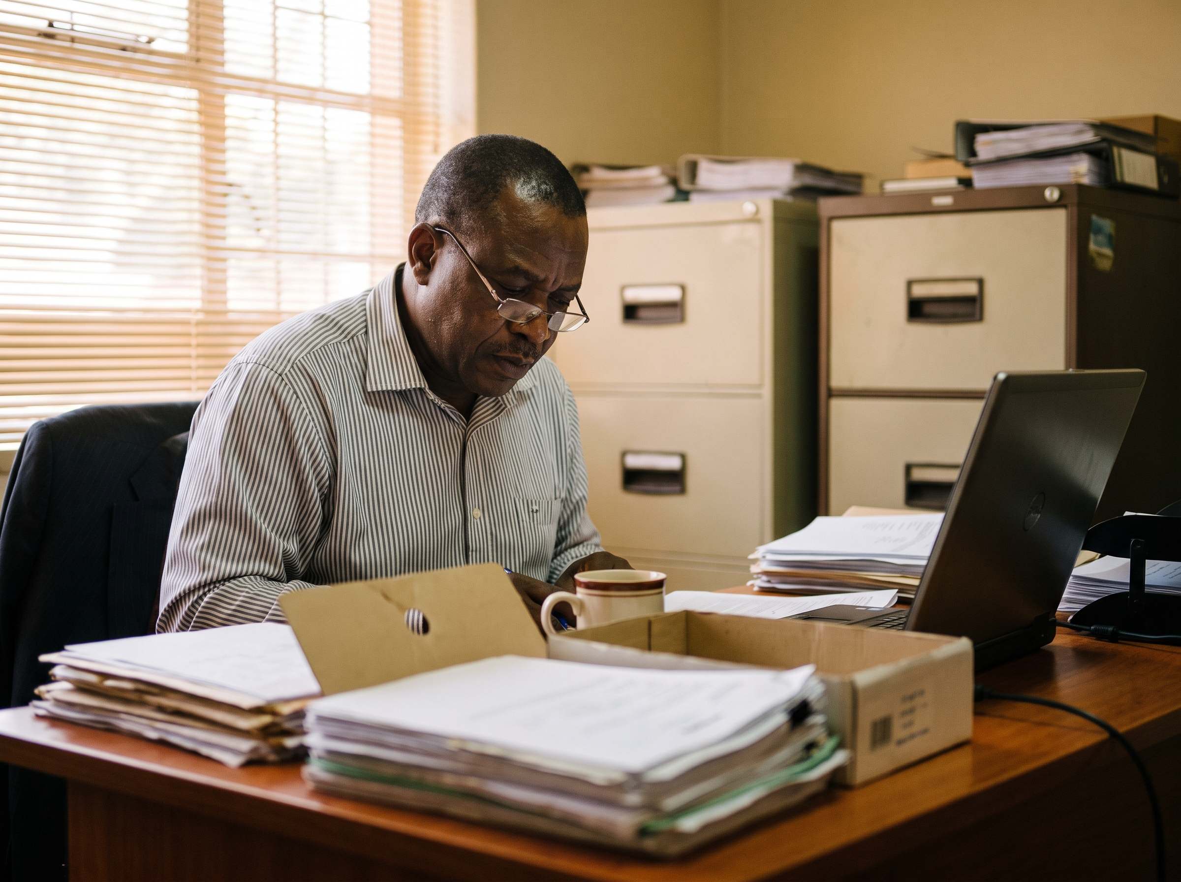 An accountant working at a desk in the Longacres office, papers and a box file open.
